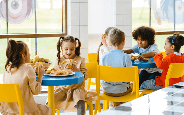 A group of children sitting at tables eating food.