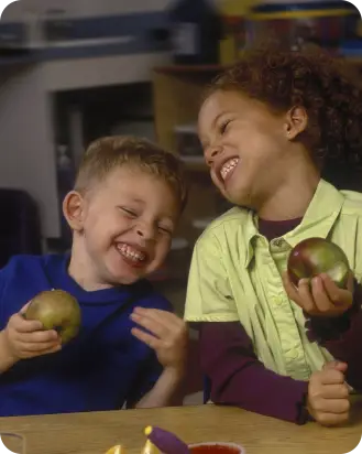 Two children are holding apples and laughing.