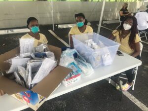 Two women wearing masks sit at a table with boxes of supplies.